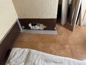 雑居ビルの階段巾木に開いた大きな穴。内部の下地まで損傷が見られる状態。