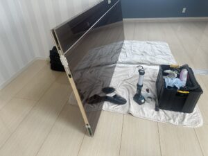 メンテナンスのために取り外された重たい引き戸と、床に広げた工具セットと作業シート