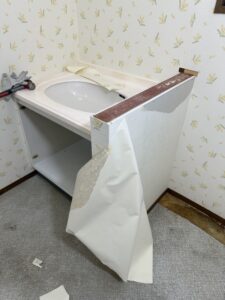 既設洗面化粧台の回りに貼られてある壁紙を丁寧に剥がしている写真