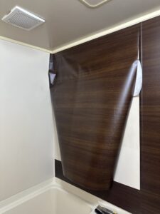 ユニットバスの壁に木目調のダイノックシートを施工中。途中段階で位置と気泡を確認している様子