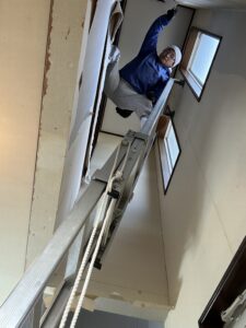 梯子の上段にて壁紙を剥がしてる様子の写真です。