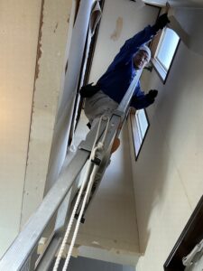 吹き抜け部壁面の壁紙を剥がしています。