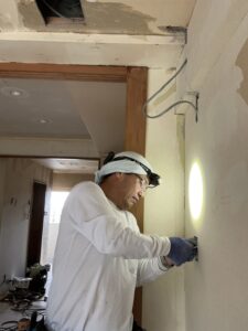 壁際でダウンライト配線作業をするリフォームアーチストの山本氏